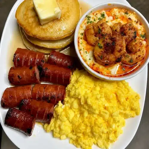 Shrimp and grits breakfast served with pancakes, sausage, and cheesy scrambled eggs